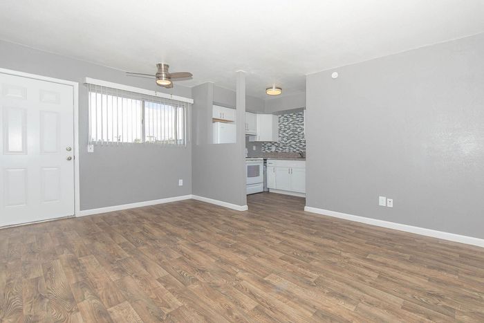 Bright modern living space featuring sleek wood flooring, large window, and an open kitchen with stylish backsplash.