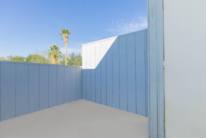 Bright and inviting outdoor space with blue-painted privacy fencing and a glimpse of lush greenery under a clear blue sky.