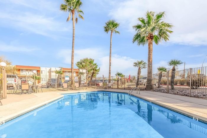 Inviting outdoor pool area with crystal blue water surrounded by palm trees and lounge seating, perfect for a relaxing day.