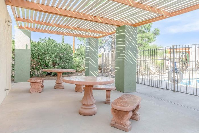 Inviting outdoor patio area with elegant stone tables and benches under a stylish pergola, perfect for relaxing near the pool.