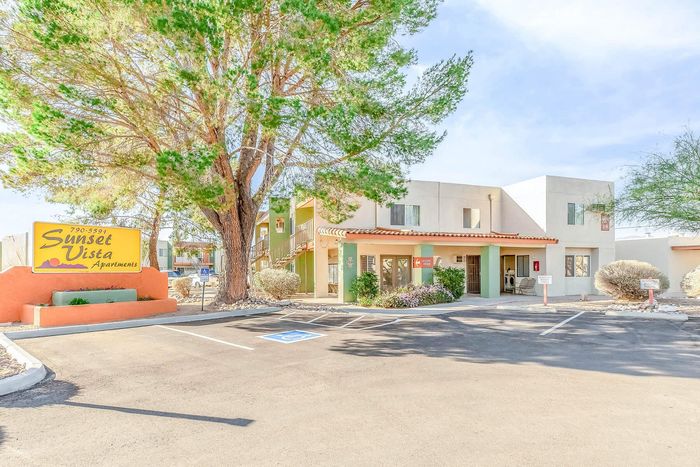 Sunset Vista Apartments with charming facade, vibrant landscaping, and spacious parking area, surrounded by lush trees and inviting entrance.