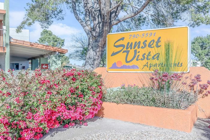 Vibrant Sunset Vista Apartments sign surrounded by lush greenery and colorful flowers, creating a welcoming atmosphere.