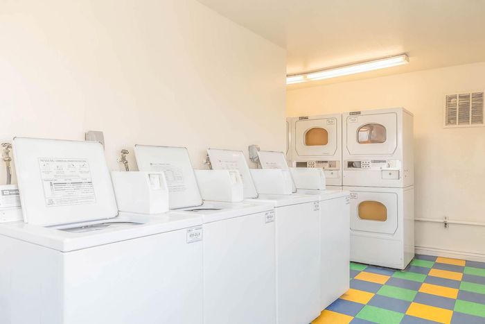 Bright and inviting laundry room with multiple modern washing machines and dryers, featuring vibrant checkered flooring.