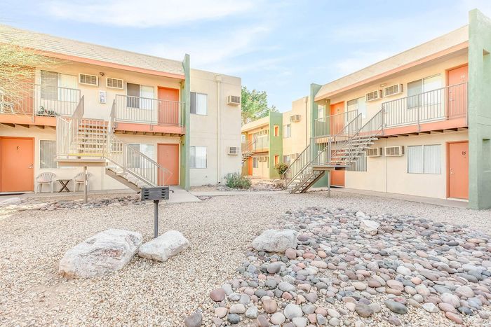 Charming apartment complex courtyard with vibrant doors, inviting staircases, and a serene landscaped rock garden under a clear blue sky.