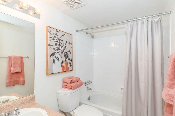 Bright and inviting bathroom with classic white tiles, modern fixtures, and elegant artwork. Features plush peach towels adding a touch of warmth and luxury.