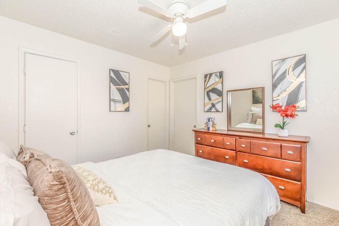 Bright, elegant bedroom featuring a cozy bed, stylish artwork, and a classic wooden dresser with a mirror, creating a serene and inviting atmosphere.