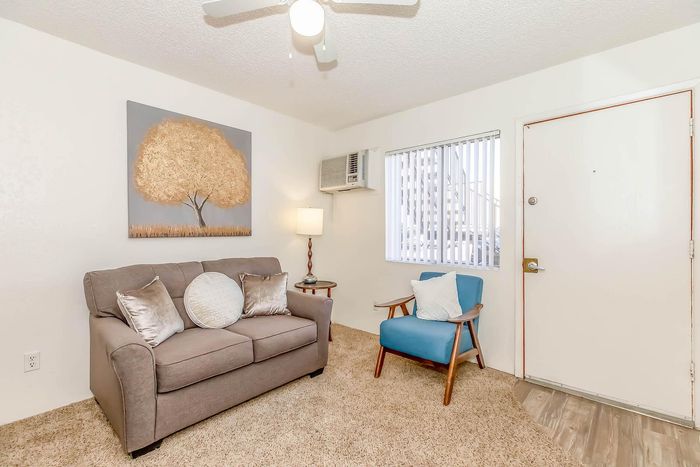 Charming living room with cozy sofa, vibrant blue accent chair, and stylish tree artwork, bathed in natural light.