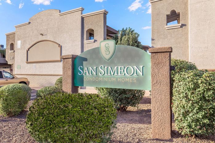 Inviting entrance to San Simeon Condominium Homes with lush green landscaping and elegant signage.