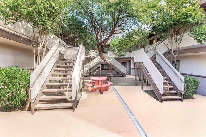 Inviting courtyard with dual staircases, lush greenery, and a charming red picnic table under a shaded tree.