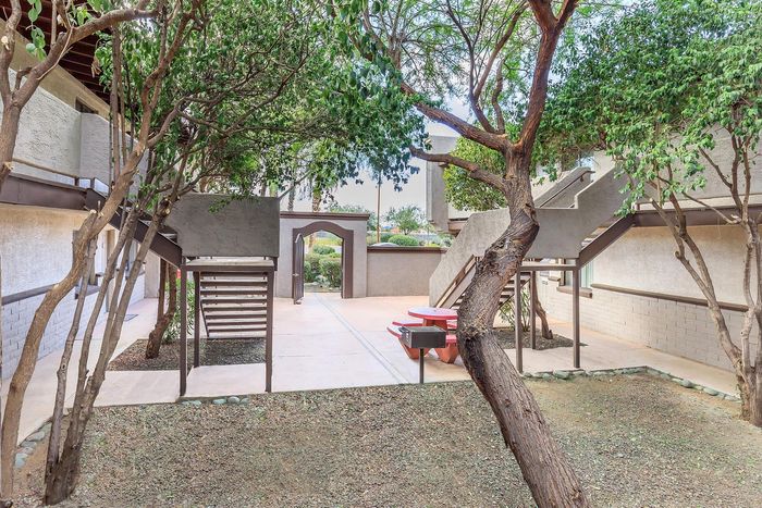 Charming apartment entrance with lush greenery, a stylish patio area, and modern staircases.