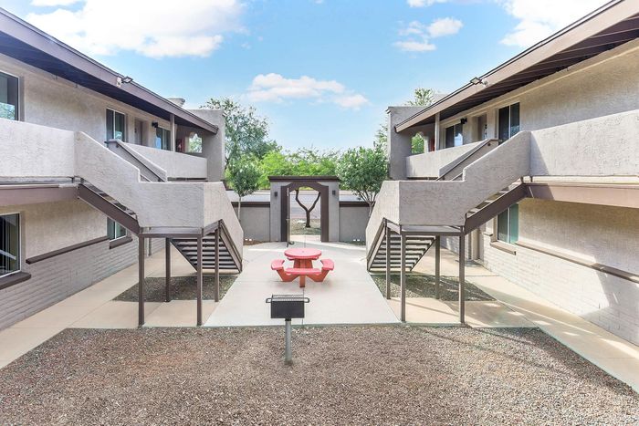 Charming courtyard with modern staircases and a vibrant red picnic table, surrounded by contemporary architecture and lush greenery.