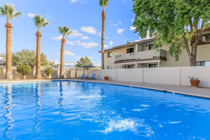 Inviting outdoor swimming pool surrounded by palm trees and modern apartment building under a sunny sky.