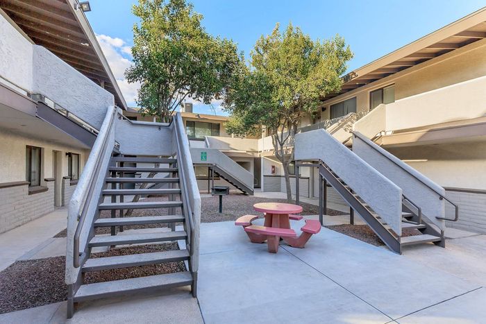Charming apartment courtyard featuring modern staircases, lush greenery, and a cozy picnic area with stylish seating.