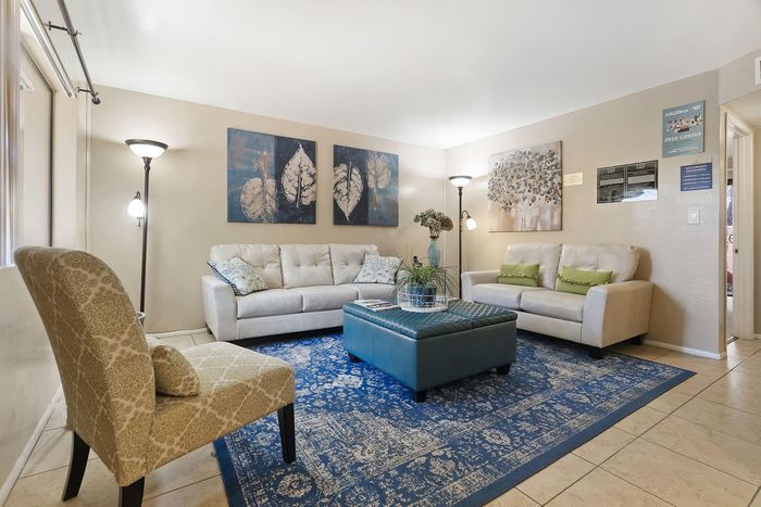 Inviting living room with elegant decor, featuring plush sofas, a patterned armchair, a stylish blue ottoman, and captivating wall art.
