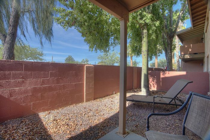 Charming outdoor patio with relaxing lounge chairs, shaded by lush trees and surrounded by a cozy privacy wall.