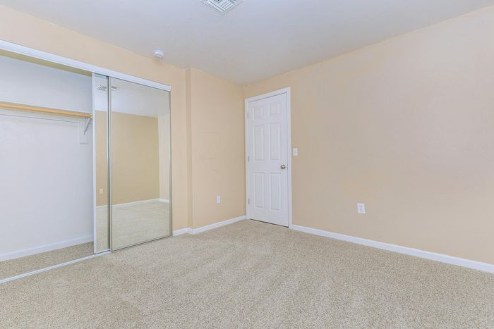 Bright, freshly-painted room with plush carpet and mirrored sliding closet doors, perfect for a spacious and modern bedroom.