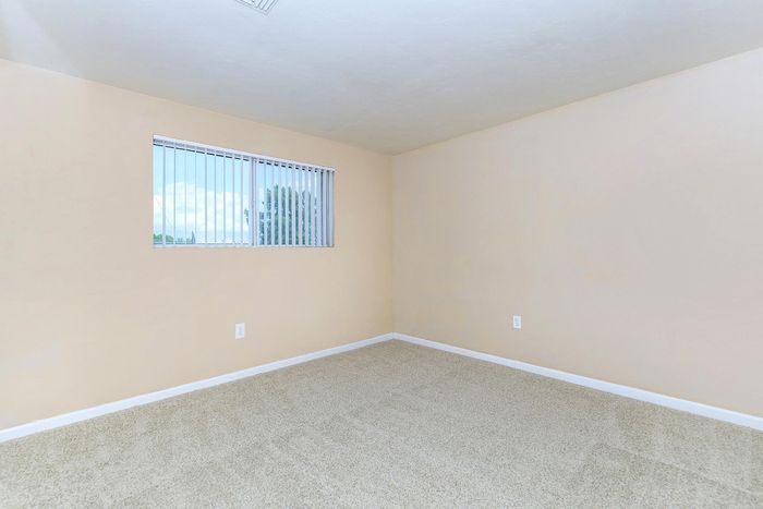 Bright and airy room with plush carpeting, neutral walls, and a large window offering serene views, perfect for a cozy bedroom or home office.