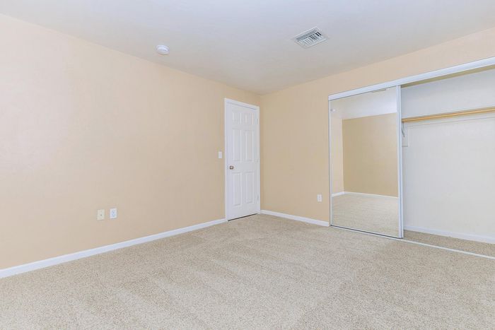 Bright and spacious bedroom with plush carpet and large mirrored closet doors.
