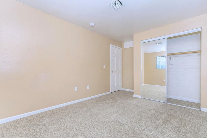 Spacious bedroom with soft beige walls, plush carpeted floor, and a large mirrored closet enhancing the room's brightness.