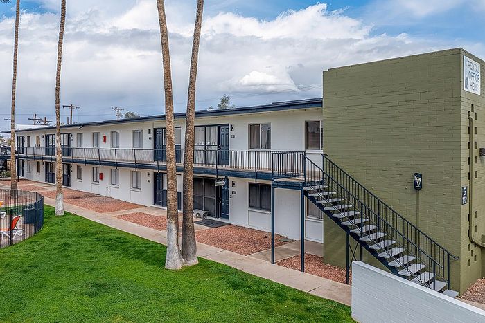 Charming two-story apartment complex with lush green lawn, tall palm trees, and outdoor stairs leading to the second-floor balconies.
