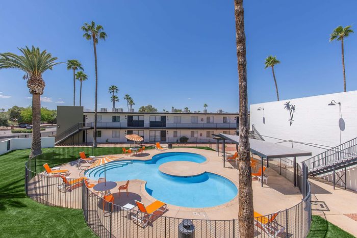 Modern apartment complex with inviting poolside area, surrounded by stylish orange lounge chairs and vibrant palm trees.