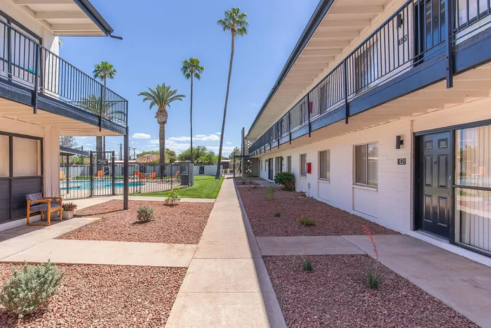 Contemporary apartment complex with beautifully landscaped pathways and a refreshing pool area, accented by vibrant greenery and tall palm trees.
