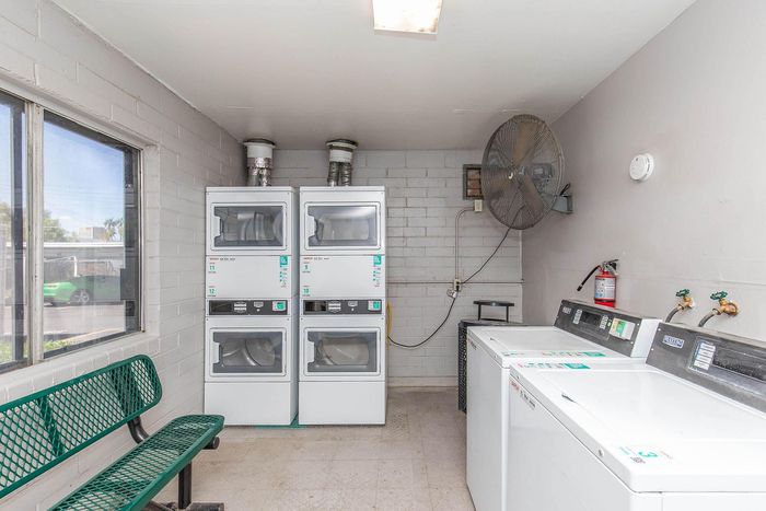 Bright and airy laundry room equipped with modern washers and dryers, large fan, bench seating, and ample natural light.