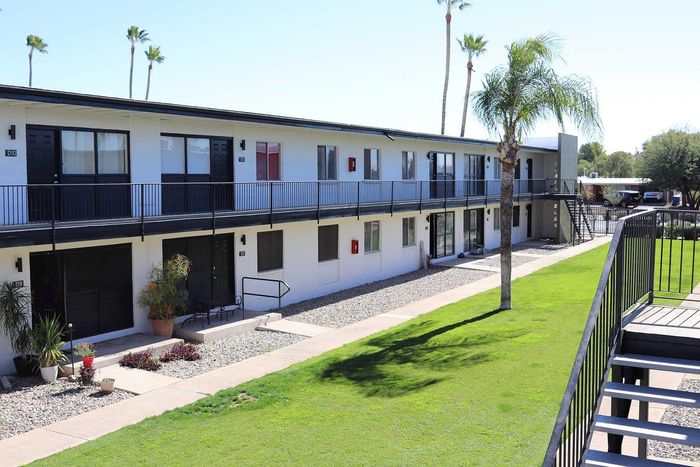 Charming apartment complex showcasing modern two-story buildings with balconies, surrounded by lush green lawns and palm trees, perfect for serene living.
