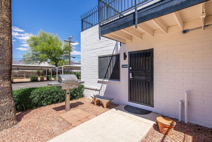 Inviting outdoor space featuring a stainless steel barbecue grill and entrance to a laundry room, with clear blue skies and lush greenery enhancing the vibrant atmosphere.