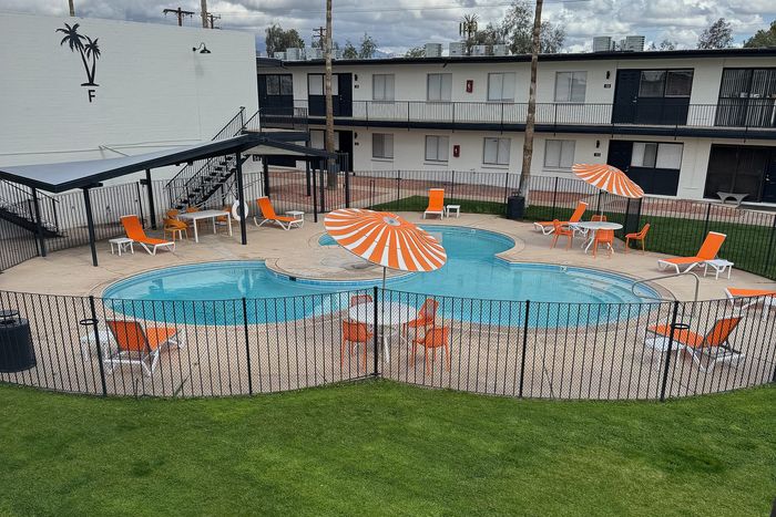 Inviting pool area with vibrant orange loungers and umbrellas, set within a well-kept courtyard, offering a perfect space for relaxation and social gatherings.