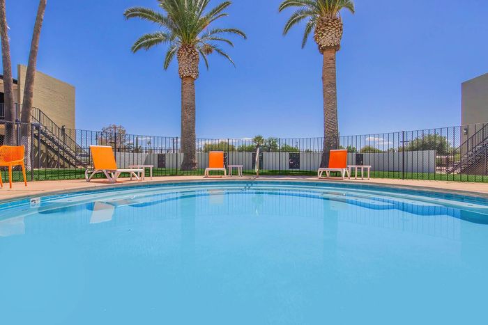 Inviting pool area with vibrant orange seating, framed by elegant palm trees and clear blue skies.