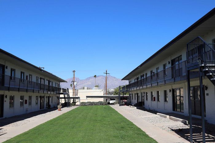 Charming apartment complex with lush green courtyard, surrounded by modern two-story buildings and scenic mountain views in the background.