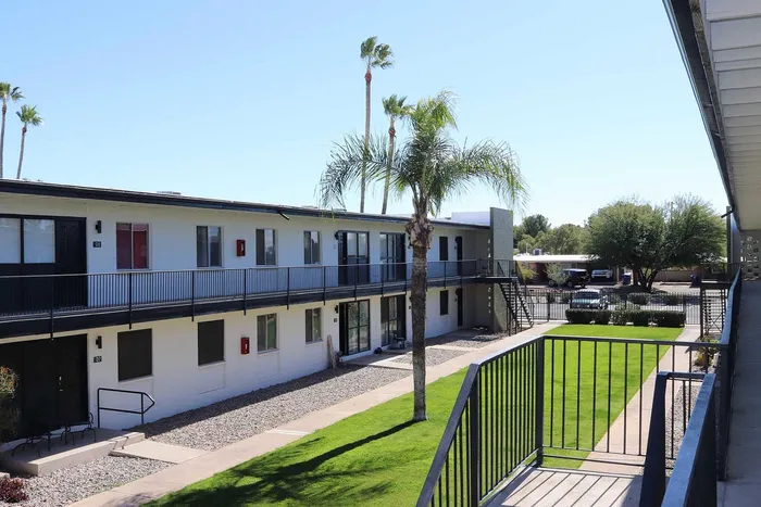 Charming apartment complex featuring modern two-story buildings, lush green lawns, and swaying palm trees under a clear blue sky.