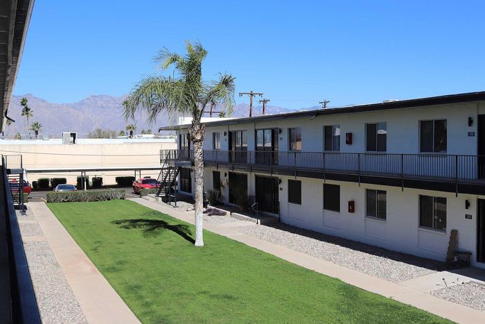 Charming apartment complex with palm trees, manicured lawn, and stunning mountain views under a bright blue sky.