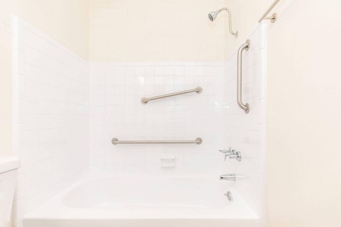 Pristine bathroom featuring an elegant white bathtub with modern safety grab bars and a sleek showerhead.