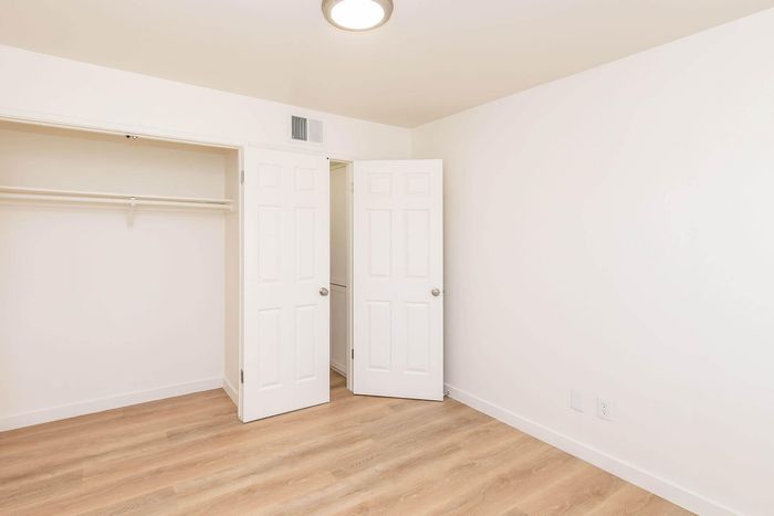 Bright and airy bedroom with pristine white walls, elegant wooden floors, and a spacious open closet perfect for modern living.