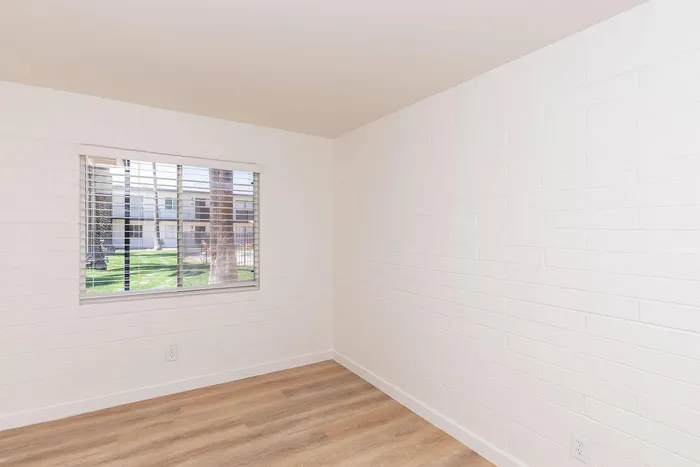 Bright, minimalist room with sleek wooden flooring and a large window offering a delightful outdoor view, ideal for creating a cozy living space.
