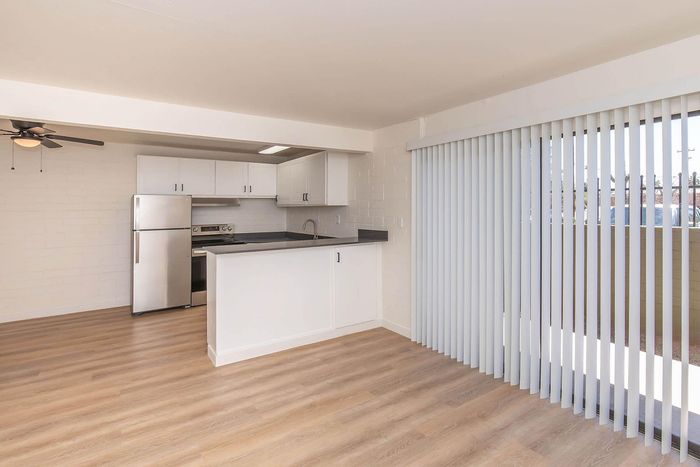 Bright and modern kitchen with stainless steel appliances, white cabinetry, and sleek countertops, featuring large floor-to-ceiling windows with elegant vertical blinds.
