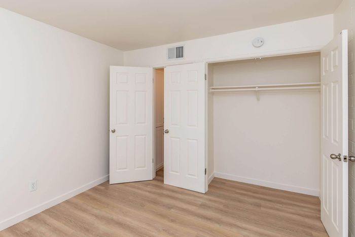 Bright and spacious bedroom with sleek wood flooring, featuring ample closet space and modern double doors.