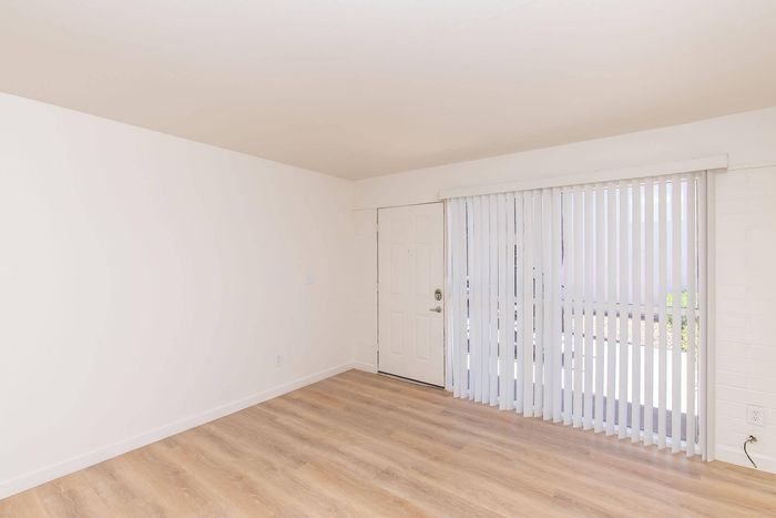 Bright and airy room with sleek laminate flooring, large window with vertical blinds, and modern entry door.