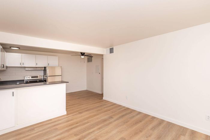 Bright, modern kitchen with sleek white cabinets and stainless steel appliances, complemented by warm wooden flooring and a ceiling fan.