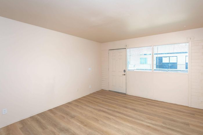 Bright and welcoming living space with elegant wood flooring, large window for natural light, and easy access door.