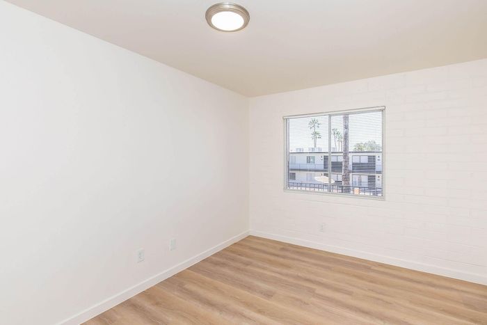 Bright and airy room featuring elegant hardwood floors, a large window with blinds, and pristine white walls.