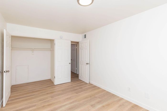 Bright and inviting bedroom featuring elegant wood flooring, ample closet space, and fresh white walls.