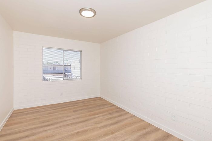 Bright, modern room with sleek white walls and stylish wooden flooring, offering a clear view through a sunlight-filled window.