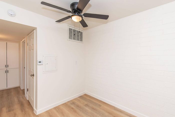 Bright and airy room featuring elegant wooden flooring, a modern ceiling fan, and ample closet space in a contemporary apartment.