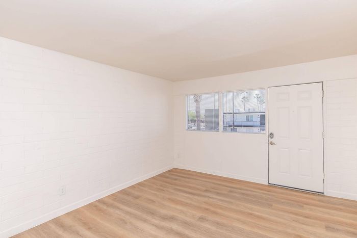 Bright, minimalist room with sleek wood flooring, large window for natural light, and modern white walls, offering a welcoming and spacious feel.