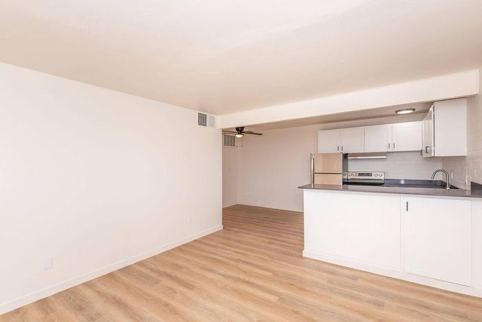 Modern open-plan living space featuring sleek wooden flooring and a stylish kitchen with white cabinetry and stainless steel appliances.