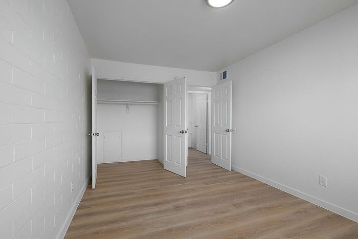 Bright, spacious room with modern wooden flooring and white walls, featuring a large closet with double doors.