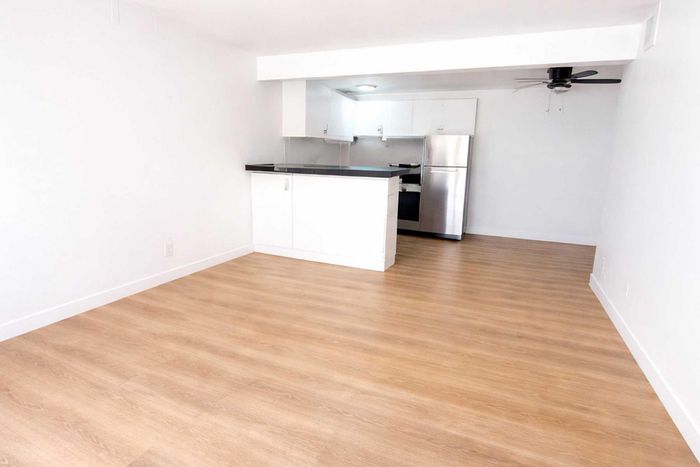 Modern apartment kitchen with sleek white cabinets, stainless steel fridge, and elegant wood flooring.